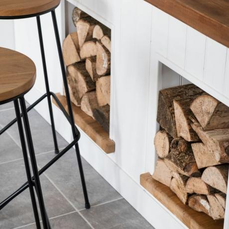 Wit keukeneiland met houten aanrechtblad en nissen voor houtblokken, hout en zwart metalen krukken