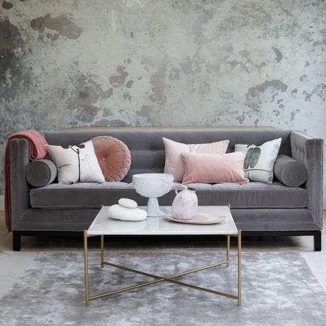 Šedý obývací pokoj s kovově šedou tapetou a elegantní šedou sametovou pohovkou s růžovými polštáři