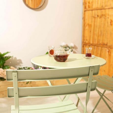 Mesa de bistrô verde sálvia e cadeiras com café no jardim.