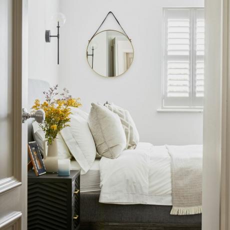 Oglindă circulară suspendată deasupra patului, cu lenjerie de pat și perne albe