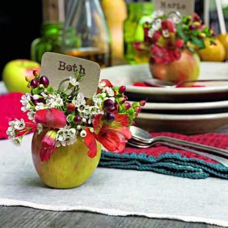 Una mesa con tarjetas para sentarse, adornos florales y de manzanas.