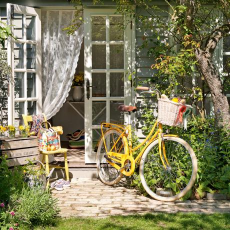 un jardín con hierbas y follaje maduro con una casa de verano y una bicicleta amarilla - tim young