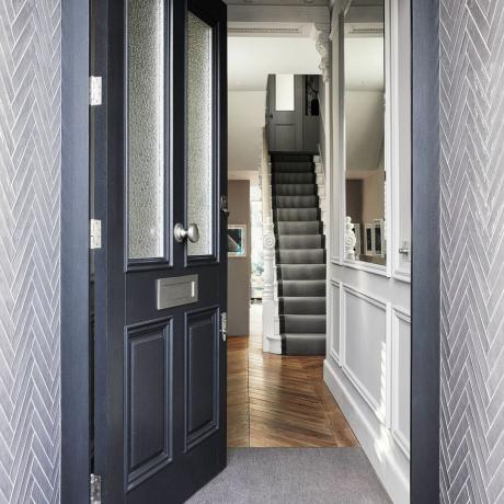 Open voordeur die leidt naar een hal met klassieke bladpleisterversiering en een trap met getextureerd grijs tapijt