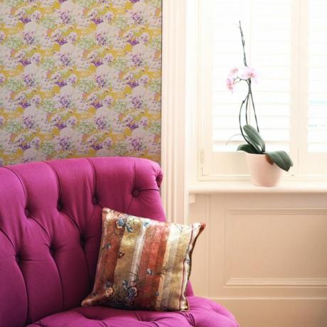 Karštai rožinis fotelis šalia skaidraus šoninio stalo ir orchidėjos, dekoruotas prancūzišku stiliumi