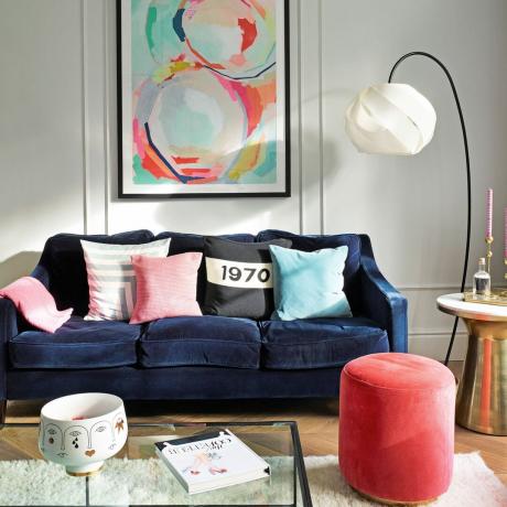 dnevni boravak sa zidnom umjetnošću, tamnoplavom baršunastom sofom, ružičastim baršunastim stolcem i razbacanim jastucima, lučnom svjetiljkom