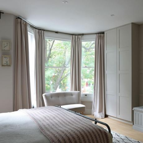 غرفة نوم رئيسية مع نافذة كبيرة منحنية وخزائن ملابس مُجهزة