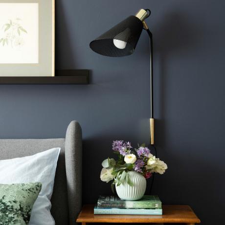 Tumši zila guļamistaba ar lasīšanas gaismu pie sienas