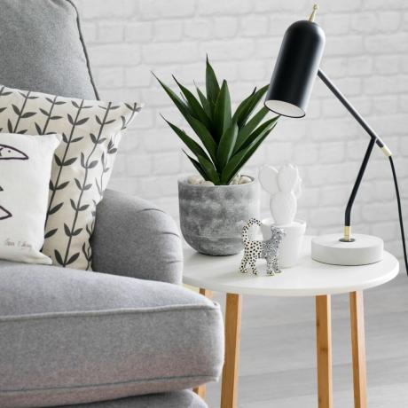grå soffa med mönstrade kuddar bredvid vitt litet bord med växt, bordslampa och dekor