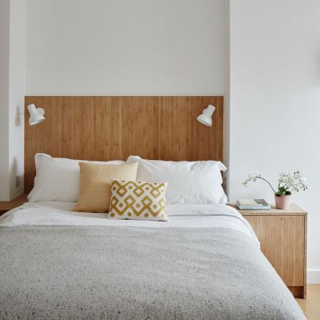 sovrum med sänggavel i trä med inbyggda sänglampor och matchande nattduksbord vitt och grått sänglinne