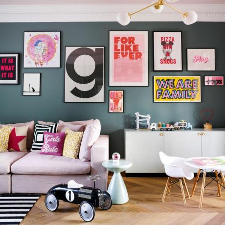породична соба са тамноплавим зидовима и зидом галерије са принтовима розе софа и дечији сто и столице