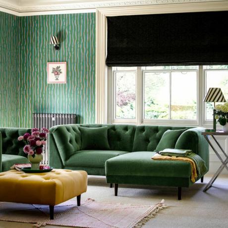 Divano verde scuro, grande finestra, pareti dipinte di verde nel soggiorno