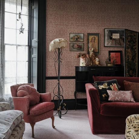幅木の色のアイデア、濃いピンクの壁紙を備えたビクトリア スタイルのリビング ルーム、ソファと肘掛け椅子、黒い木工品と幅木、レースのカーテン、ヴィンテージのアートワーク