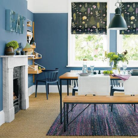 Blå spisestue med blomstrede persienner, sisal-tæppe og stenpejs