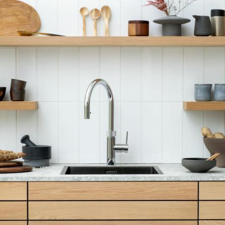 Robinet argintiu de apă clocotită instantanee pe blatul alb de bucătărie cu dulapuri din lemn