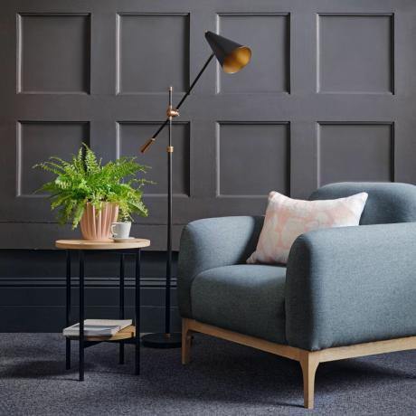 blå enkelsoffa med dekorativt bord, lampa och grå väggpanel