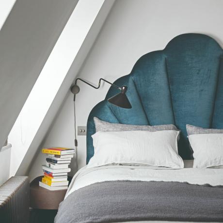 Bett mit grau-weißer Bettwäsche und marineblauem Kopfteil, daneben Nachttisch mit Büchern