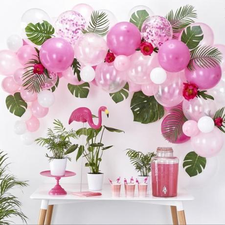 atogrąžų tematikos vakarėlio baliono arka virš stalo su rožiniu flamingo ir gėrimų dozatoriumi