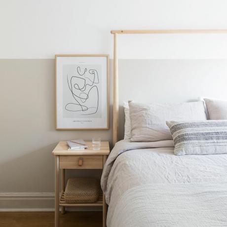 Dormitorio neutro con sábanas de lino en la cama junto a una mesa de madera.