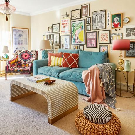 Vardagsrum med stor turkos soffa, gallerivägg och svängt soffbord