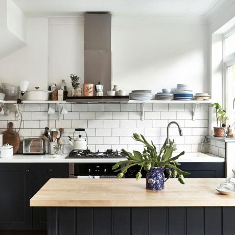 virtuvė su baltomis plytelėmis ir juoda spintele bei ištraukimo ventiliatoriumi