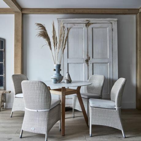 등나무 의자, 원형 테이블, 장식장, 테이블 위의 꽃병, 나무 바닥 보드가 있는 중성 옅은 회색 식당