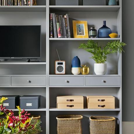 קיר מדפים פתוחים בסלון צבוע באמצע אפור עם מקום לטלויזיה ואפשרויות אחסון שונות