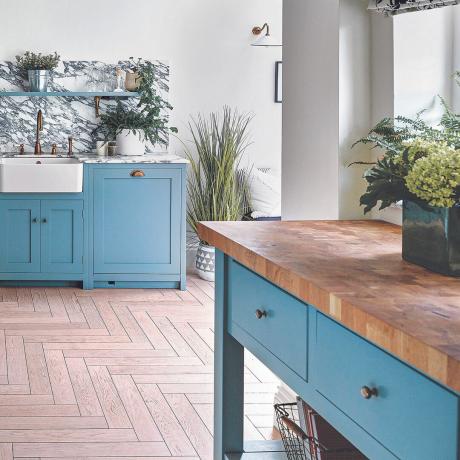 Bucătărie cu dulapuri albastru deschis și insulă de bucătărie albastră de sine stătătoare cu blat din lemn.