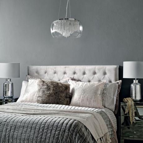 Glam pilkas miegamasis su šviesiai pilka apmušta galvūgaliu ir prabangiais šviestuvais prie lovos bei pakabuku