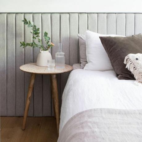 Бело окречена спаваћа соба са тапацираним зидним облогама узглавља, дрвеним округлим столом