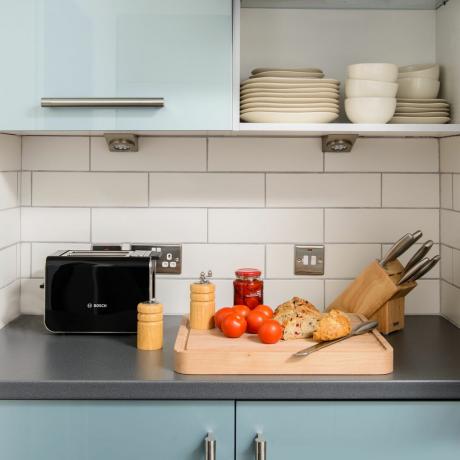 Кухонная стойка с тостером, блоком ножей и разделочной доской с овощами.