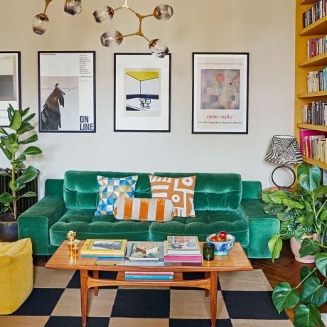 أريكة خضراء في غرفة المعيشة مع طاولة قهوة قديمة ومطبوعات على الحائط