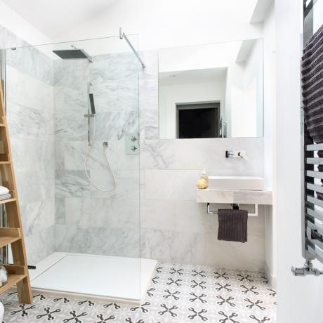 Baño pequeño con mampara de ducha de vidrio abierta, azulejos de mármol y baldosas estampadas