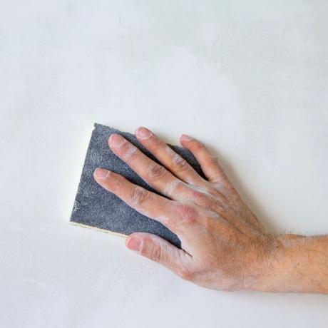 lijar a mano una pared blanca con papel de lija