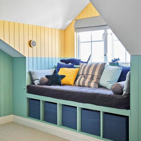 ที่นั่งริมหน้าต่างห้องนอนพร้อมผนังกรุทาสีฟ้าและเหลือง