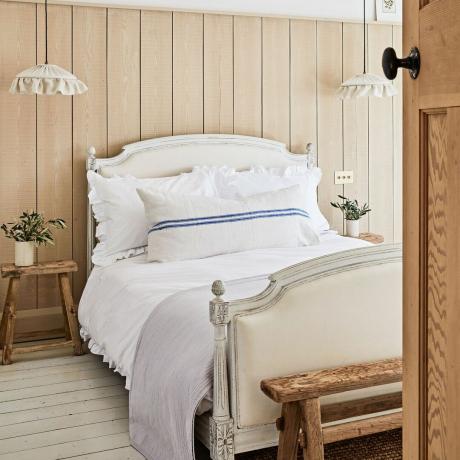 Sypialnia z drewnianym i tapicerowanym łóżkiem w stylu vintage oraz ścianami wyłożonymi boazerią