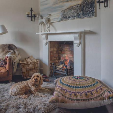 Un rincón de la sala de estar con un fuego abierto en una chimenea, un sillón de cuero y una alfombra de piel de oveja.