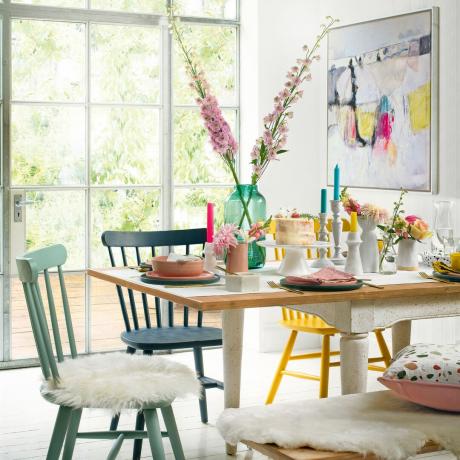 Koka galds, ko ieskauj spilgti krāsoti ēdamistabas krēsli