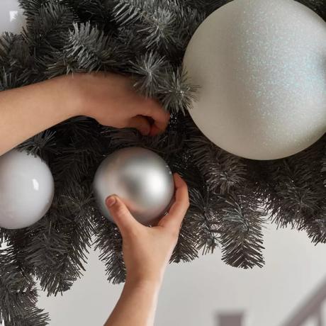 Close-up van een kerstslinger die een middelgrote zilveren kerstbal met grote witte kerstballen toevoegt
