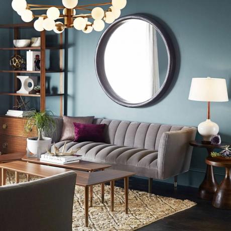 сірий диван, велике кругле дзеркало, сині стіни, багато освітлення