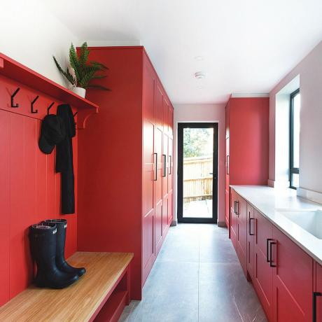 Червено мокро помещение с бяла керамична мивка, пейка за ботуши и сиви подови плочки