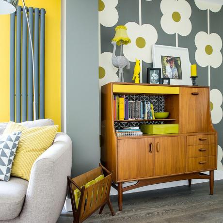 Ruang tamu terbuka yang didekorasi dengan warna abu-abu dan kuning dengan wallpaper bergaya retro