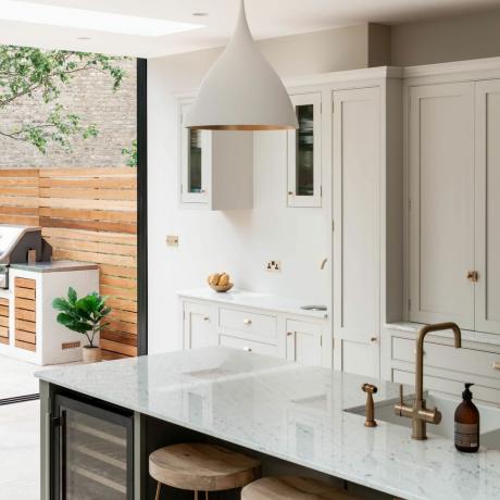 Offene Wohnküche mit Kücheninsel und Barhockern sowie einem Dachfenster und Schiebetüren, die in den Weinkühlschrank im Garten führen