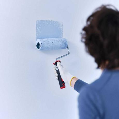 човек рисува синя стена с валяк