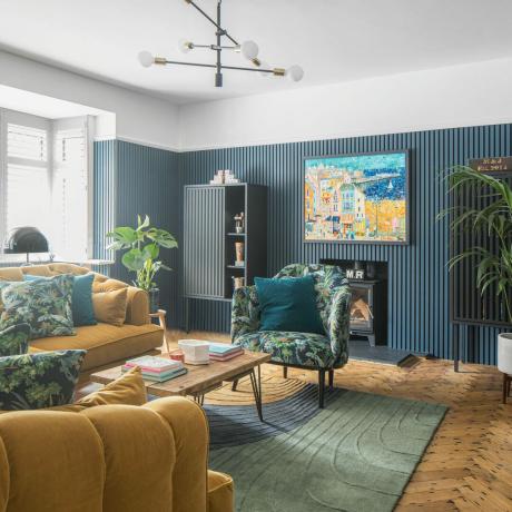 Olohuoneessa sininen panelointi ja sinapinkeltainen sohva ja tuolit