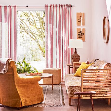ružová obývačka s prútenou pohovkou a čalúneným kreslom hrdzavej farby