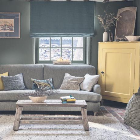 nyaman dengan dinding hijau dan sofa gelap dipadukan dengan kabinet kuning dan sofa abu-abu Morris & Co