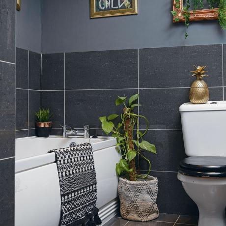 Sort badeværelse med hvidt badekar, sort toiletsæde, monokrom bademåtte, sorte klinker, stueplante