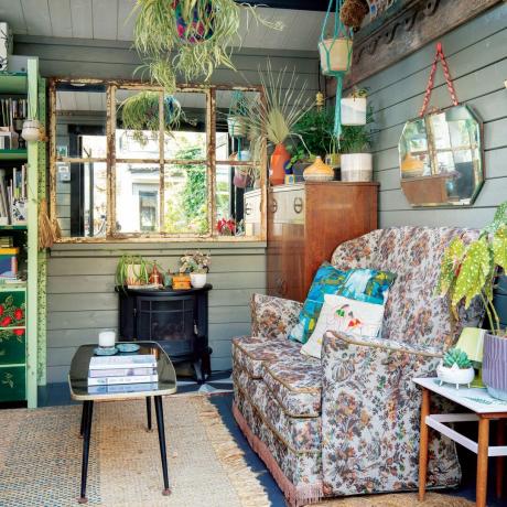 Havekontor med vintage sofa, vægpaneler, vinduesspejl, brændeovn og hængende plantekasser
