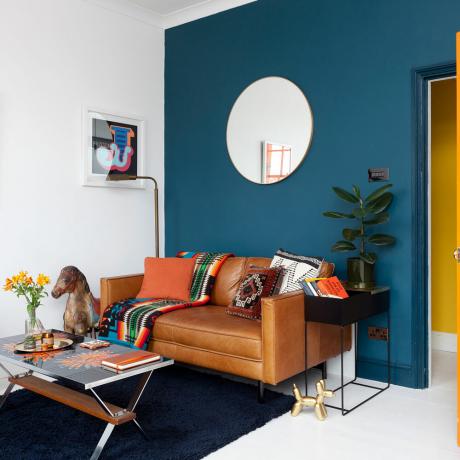 dzīvojamā istaba ar tumši zilu sienu un apaļu spoguli